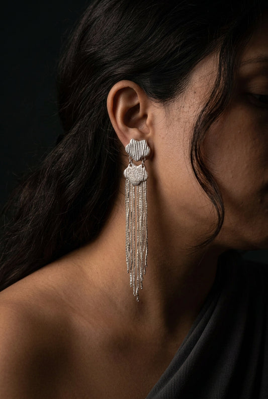 A close-up lifestyle shot of a woman wearing a long, silver-toned dangle earring with a white floral cluster at the top and cascading rhinestone-like strands.