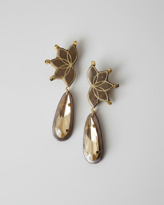 Pair of gold floral earrings with teardrop-shaped drops on a beige fabric background