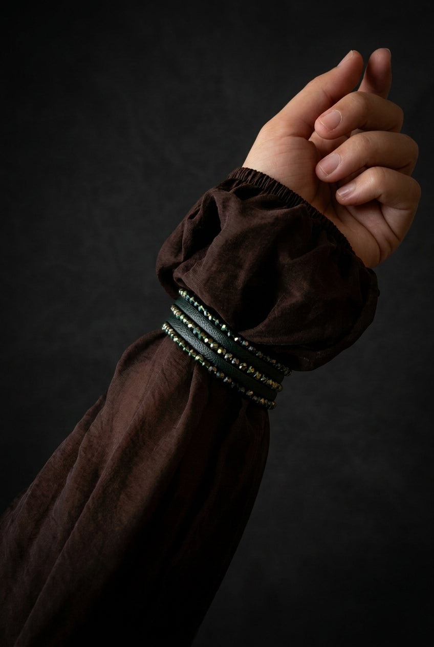 A close-up of a person's hand and forearm wearing a dark brown sheer puff sleeve with a decorative beaded cuff, set in a warmly lit living room interior.