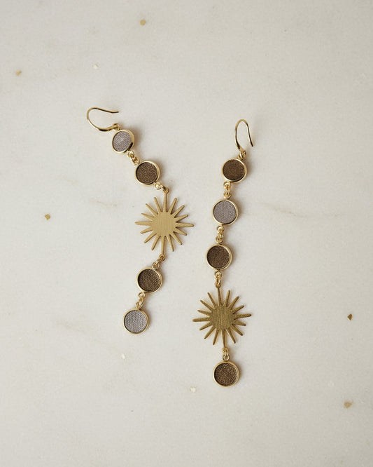 Gold sun-shaped earrings on a textured beige surface