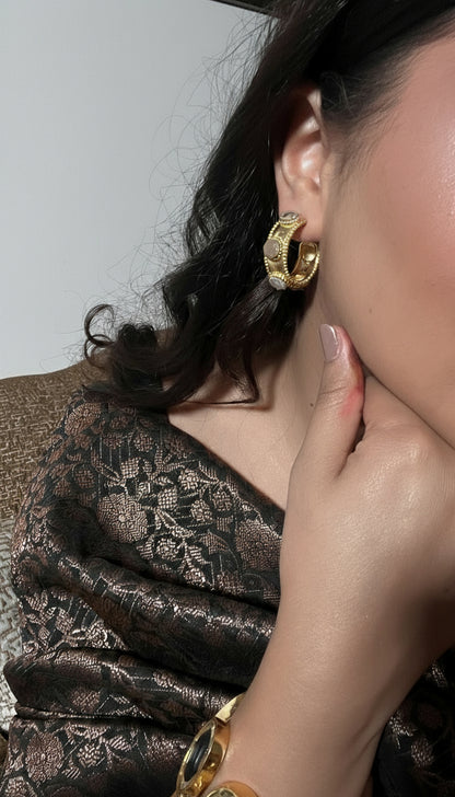 Close-up of a person wearing gold hoop earrings with a neutral background